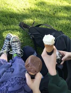 two people sitting on the grass eating ice cream and chocolate doughnuts with their feet up