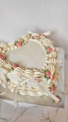 a heart shaped cake decorated with flowers and ribbons on a marble counter top, ready to be cut