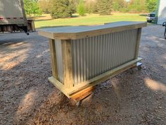 a wooden box sitting in the middle of a dirt field next to a trailer and trees