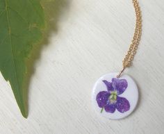 "This is my original design of a tiny, sweet violet flower. I am fascinated by violets; their deep jewel-like intense colors, delicate petals, lush heart-shaped leaves, and spindly stems. A big patch of violets comes up in our backyard every spring and when they bloom, my older daughter picks a handful for me to put in my small glass vase on the windowsill by the kitchen sink. They are the brightest color in the room! This is one of my smallest pendants; it measures 5/8\" across, smaller than a Handmade Delicate Purple Necklace, Purple Flower Charm Necklace As A Gift, Purple Flower Necklace With Charm As A Gift, Purple Flower Pendant Necklace For Birth Flower, Purple Flower Pendant Necklace With Birth Flower, Purple Birth Flower Pendant Necklace, Violet Necklace Flower, Purple Flower Necklace With Flower Charm, Handmade Purple Flower Pendant Necklace