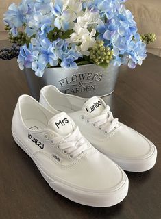 a pair of white tennis shoes sitting on top of a table next to blue flowers