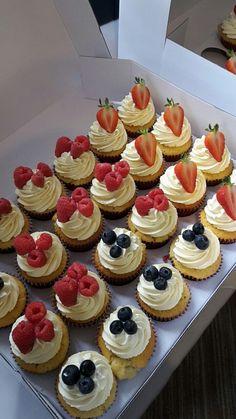 cupcakes with white frosting and strawberries on top are arranged in a box