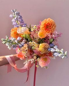 a bouquet of flowers is being held by a woman's hand with a pink ribbon