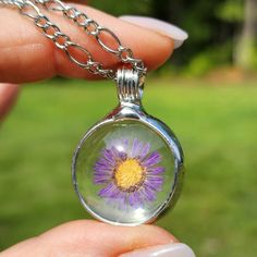 a hand holding a glass pendant with a purple flower in the center and yellow center