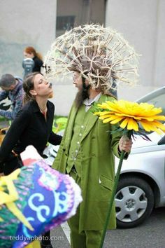 a man in a green suit with flowers on his head is standing next to a woman