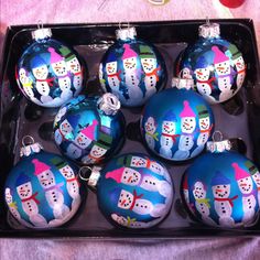 six blue christmas ornaments with snowmen painted on them in a black box next to a pink table cloth