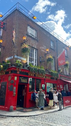 people are standing in front of a red building with plants growing on the roof and windows