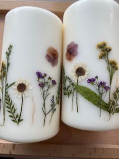 two white vases with flowers painted on them sitting on a wooden shelf next to each other