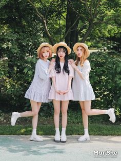 three young women standing next to each other in front of green trees and bushes with their legs crossed