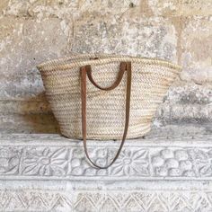 a woven basket sitting on top of a stone wall next to a wooden handled handle