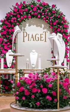 a display with pink roses and jewelry on it's sides in front of a sign that says piagei