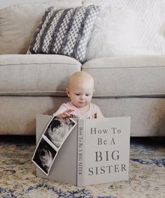 a baby sitting on the floor in front of a book