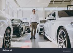 a man standing next to some cars in a showroom, looking at the camera