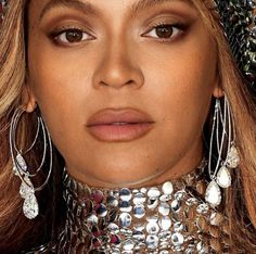 a close up of a woman wearing large earrings and necklaces on her head, looking at the camera