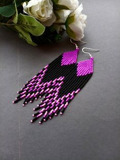 a pair of pink and black beaded earrings next to white flowers on a table