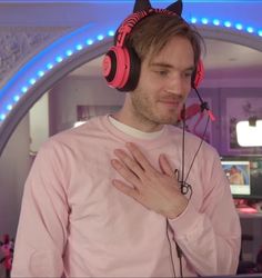 a man wearing pink headphones and holding his hands to his chest while standing in front of a mirror