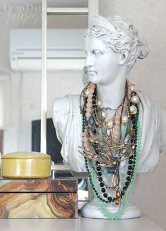 a bust of a woman with necklaces on it's neck sitting in front of a mirror