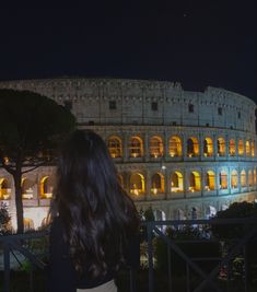 a woman standing in front of the colossion at night with her back turned to the camera