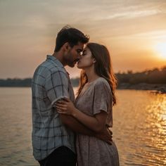 a man and woman standing next to each other in front of the water at sunset