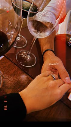 two people holding hands at a table with wine glasses