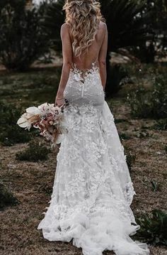 a woman in a wedding dress is walking through the grass with her back to the camera