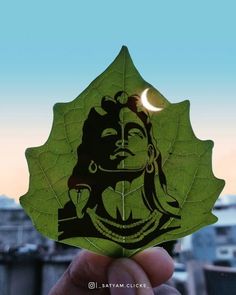 a person holding up a green leaf with a drawing on it's side and the moon in the background