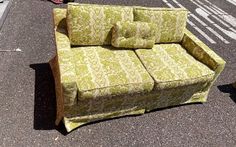 a green couch sitting on the side of a road