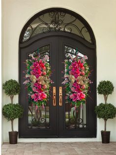 two wreaths on the front door of a house with potted plants and trees