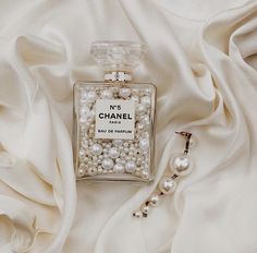 a bottle of chanel eau de parfum surrounded by white fabric and pearls