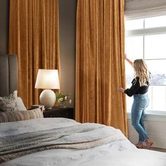 a woman standing next to a window in a bedroom