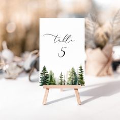 a table number card with pine trees on it sitting on top of a wooden easel