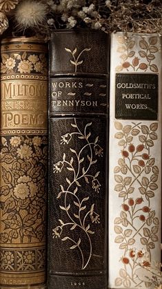 three books are lined up on a shelf with flowers in the middle and one is gold, white, and black