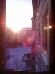 the sun shines brightly through an open window on a snowy street in front of a building