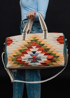 a woman is holding a handbag in front of her face and wearing blue jeans