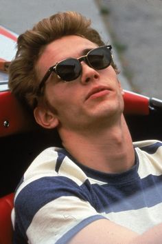 a man with sunglasses sitting in a car looking off into the distance and holding his arm out