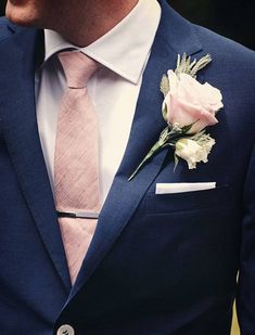 a man wearing a blue suit and pink tie with a white rose on his lapel