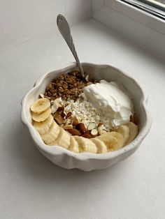 a bowl filled with yogurt, banana slices and granola next to a window