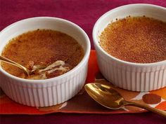 two white bowls filled with food sitting on top of a red table cloth next to gold spoons