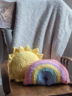 two crocheted pillows sitting on top of a wooden chair next to a blanket