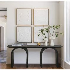 a table with vases and flowers on it in front of four framed art pieces