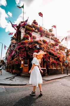 a woman walking down the street in front of a building with flowers all over it