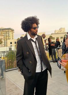 a man in a suit and tie standing on a balcony next to a woman wearing sunglasses