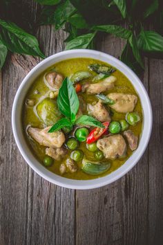 a white bowl filled with green vegetables and meats on top of a wooden table