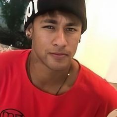 a young man wearing a red shirt and black hat is looking at the camera with an intense look on his face