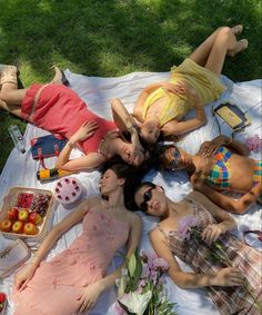 four young women laying on a blanket in the grass with food and drinks around them