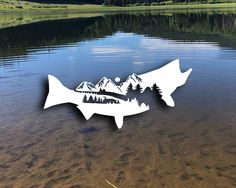 two fish cutouts sitting in the middle of a lake with mountains and pine trees