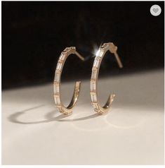 Experience the perfect blend of style and versatility with our baguette hoop earrings that come in your choice of high-quality 18K gold plated or .925 sterling silver. These exquisite earrings feature mesmerizing baguette-cut cubic zirconia, delicately encased in a radiant gold-plated hoop design. 18K Gold or .925 Sterling Silver Cubic Zirconia Baguettes Size: .81" 14k Gold Hoop Earrings With Baguette Diamonds, Luxury Hoop Earrings With Baguette Diamonds As Gift, Gold Baguette Cut Cubic Zirconia Huggie Earrings, Gold Cubic Zirconia Baguette Cut Huggie Earrings, Gold Cubic Zirconia Baguette Earrings, Luxury Baguette Diamond Hoop Earrings As Gift, Gold Sterling Silver Earrings With Baguette Diamonds, Baguette Diamond Hoop Earrings As Gift, Elegant Hoop Earrings With Baguette Diamonds