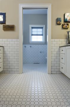 a bathroom with white tile floors and walls, along with pictures hanging on the wall