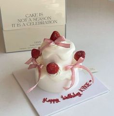 a white cake with strawberries on top sitting next to a card