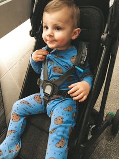 a baby sitting in a stroller with his mouth open and wearing blue pajamas, smiling at the camera